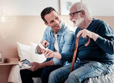 AdobeStock_200363378 - Blue Water Homecare Young man shows senior man a photograph