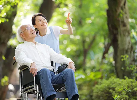 AdobeStock_82406832 - Blue Water Homecare Young woman points something out to elderly man in wheelchair