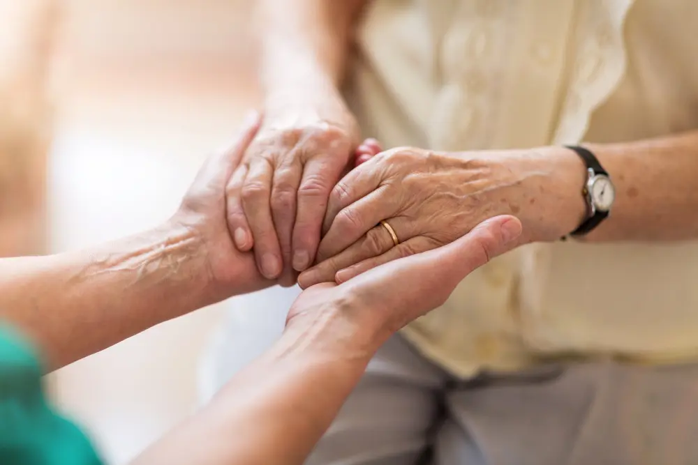 Nurse consoling her elderly patient by holding her hands - Blue Water Homecare patient and caregiver holding hands